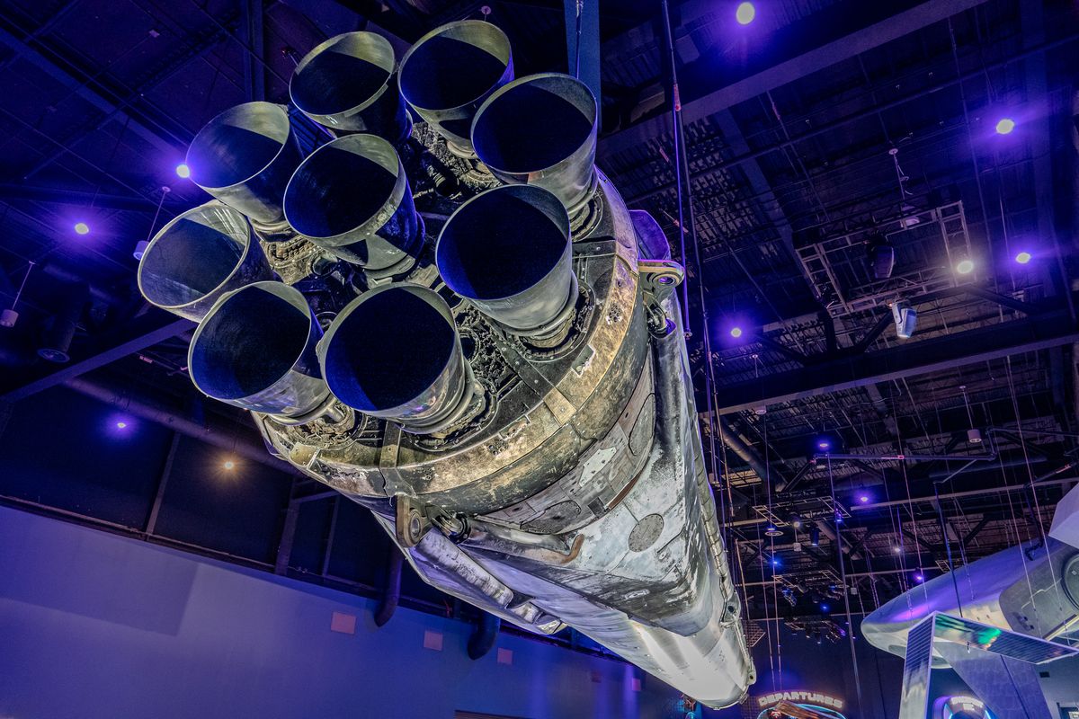 Looking up at the engine cluster of a flown rocket booster under blue exhibit lighting, Kennedy Space Center