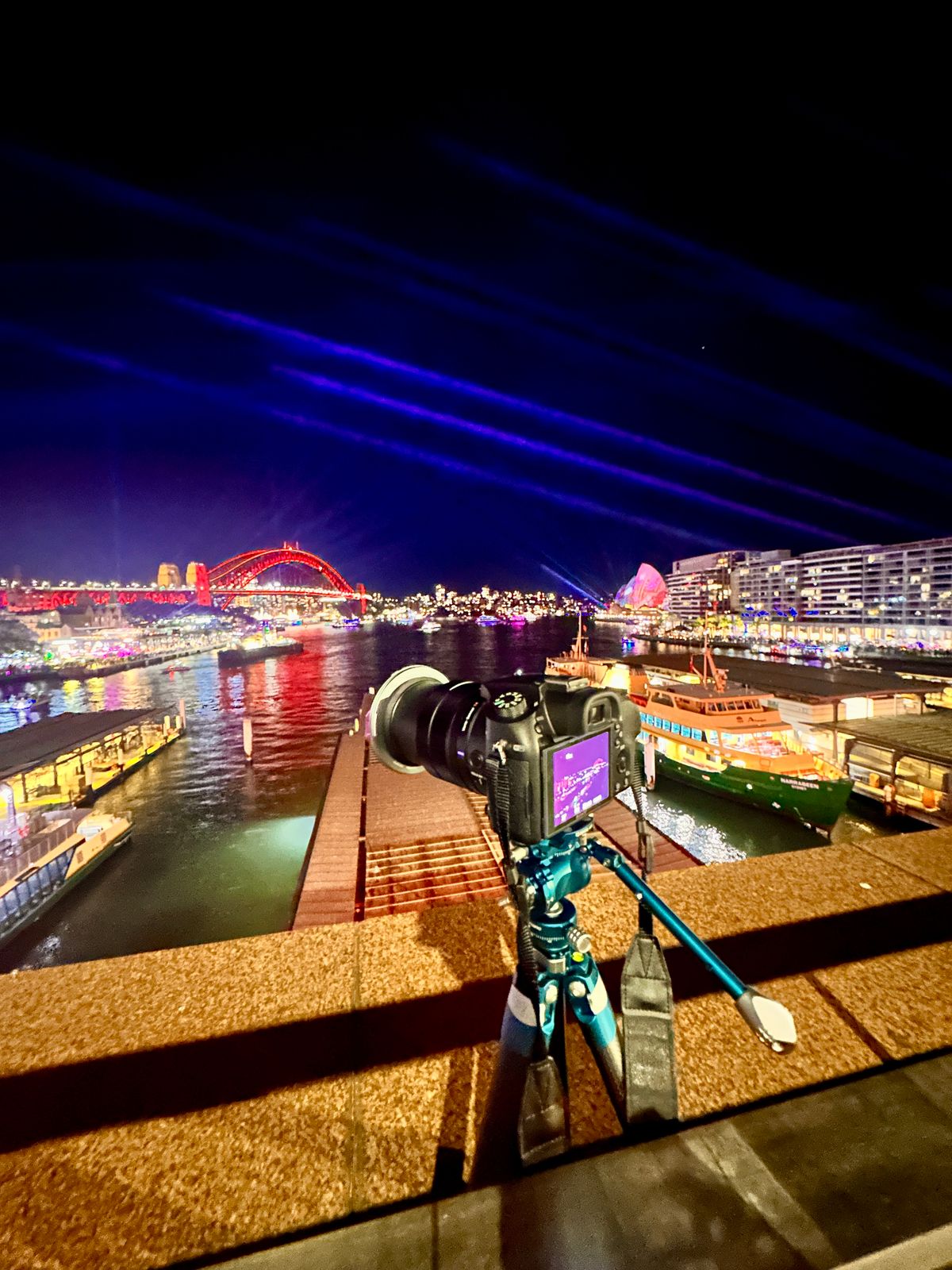 Sony RX10 IV with a NiSi filter on a blue Benro Cyanbird tripod, set up above Circular Quay during Vivid Sydney, with the Harbour Bridge lit red in the distance